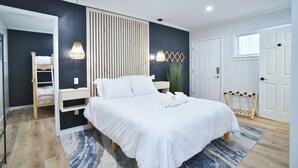 Un dormitorio con cama, lámparas de noche, una escalera de madera, una planta colgante y una puerta.