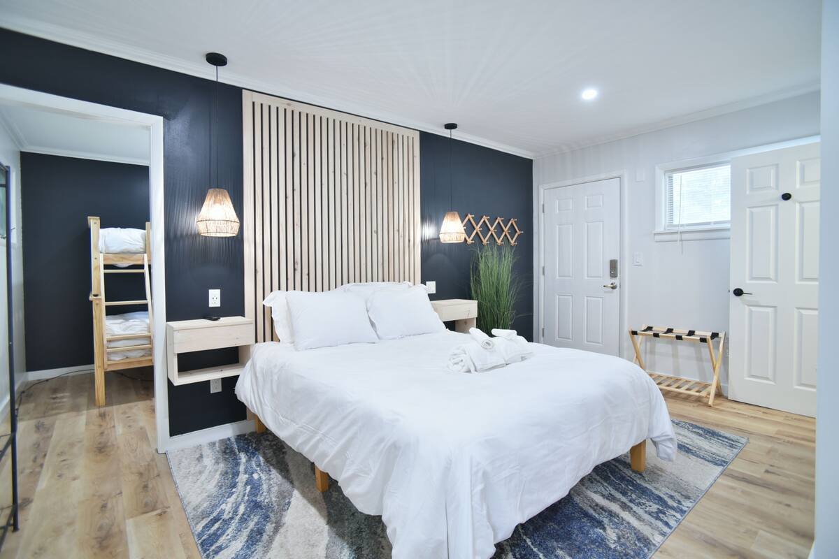 Un dormitorio con cama, lámparas de noche, una escalera de madera, una planta colgante y una puerta.