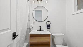 A bathroom with a white sink, a round mirror, a toilet, and a shower curtain.