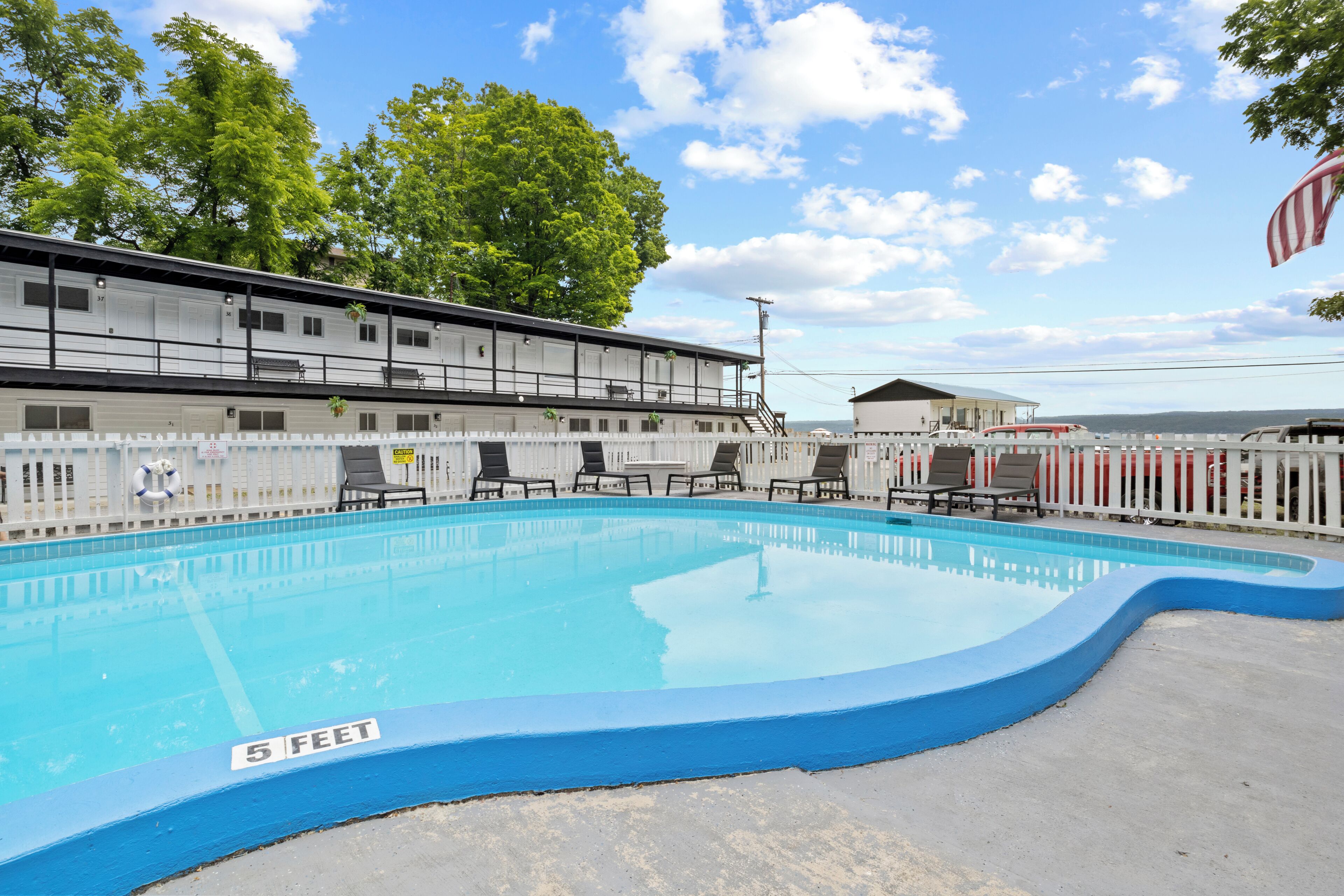Una piscina con indicador de profundidad de 1.5 metros, rodeada de sillas de descanso y una valla blanca.