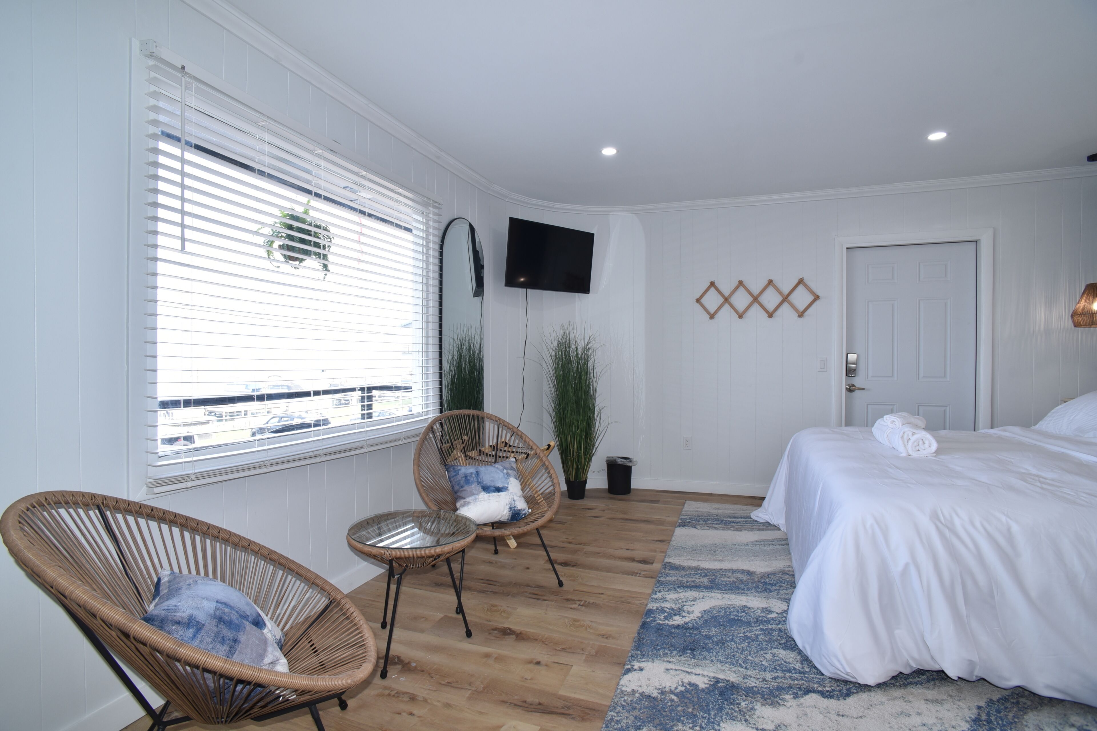 A bedroom with a bed, two wicker chairs, a TV, and a window with blinds.