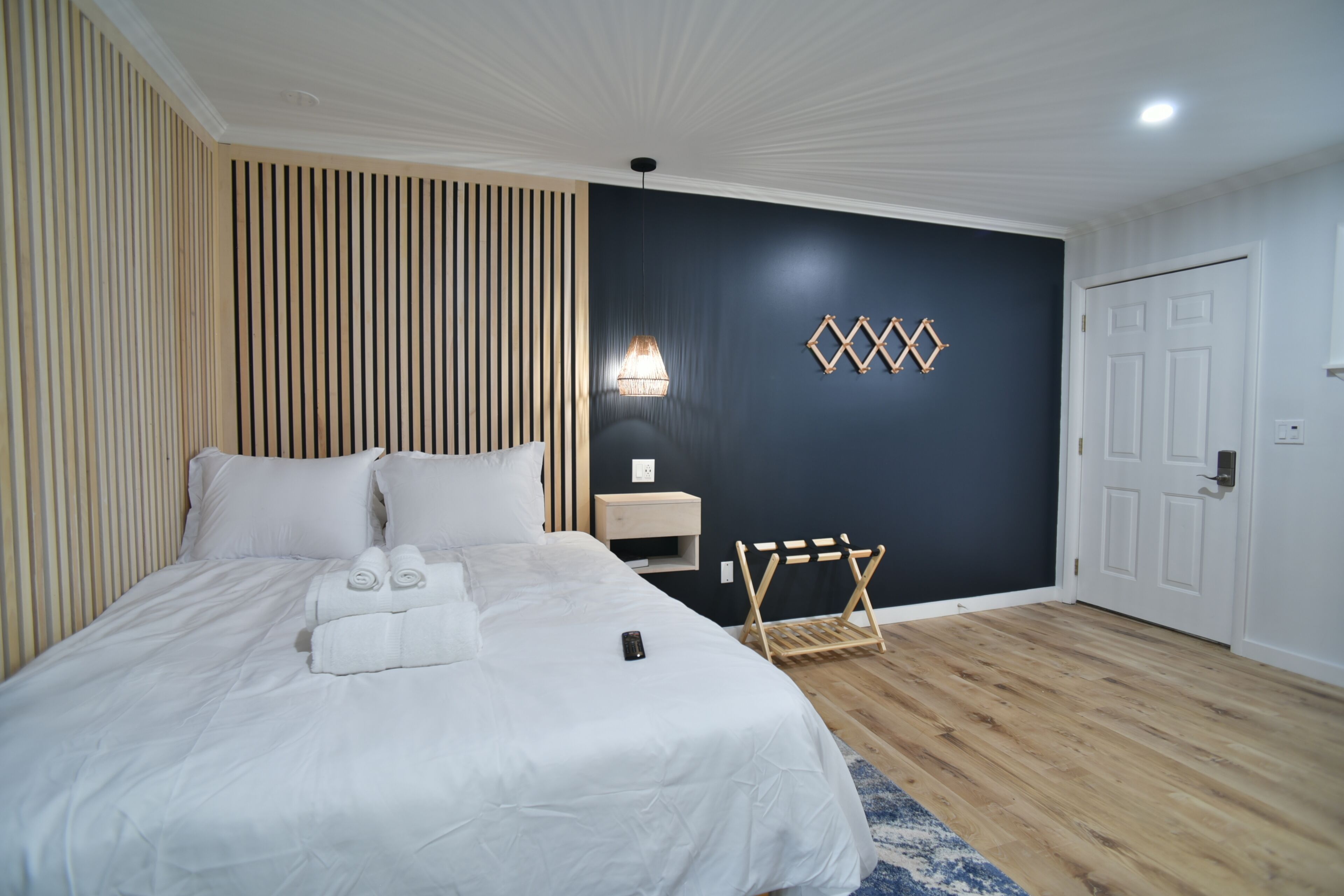 A hotel room with a bed, bedside table, lamp, and a wooden rack.