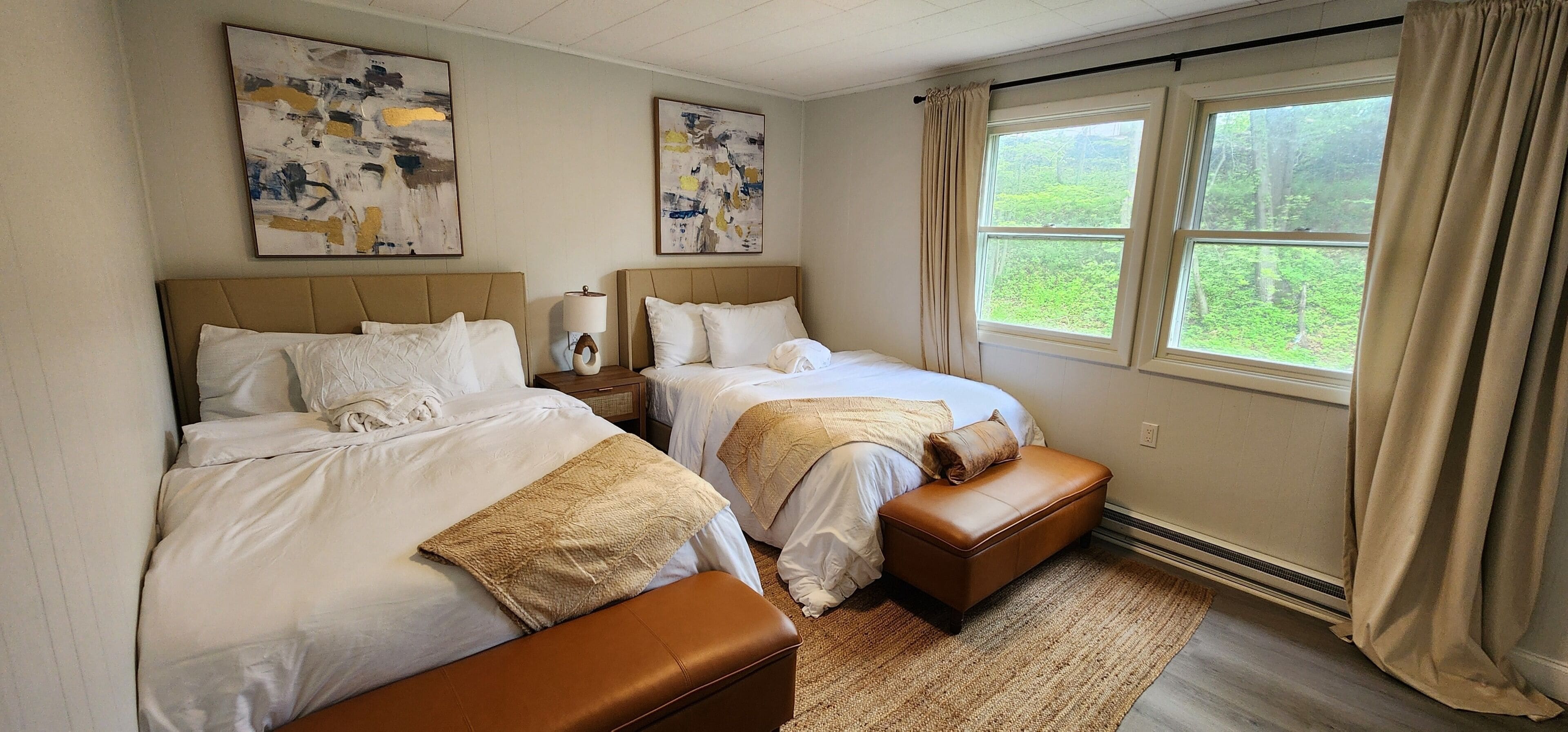 A bedroom with two beds, a nightstand, a lamp, and a window with curtains.
