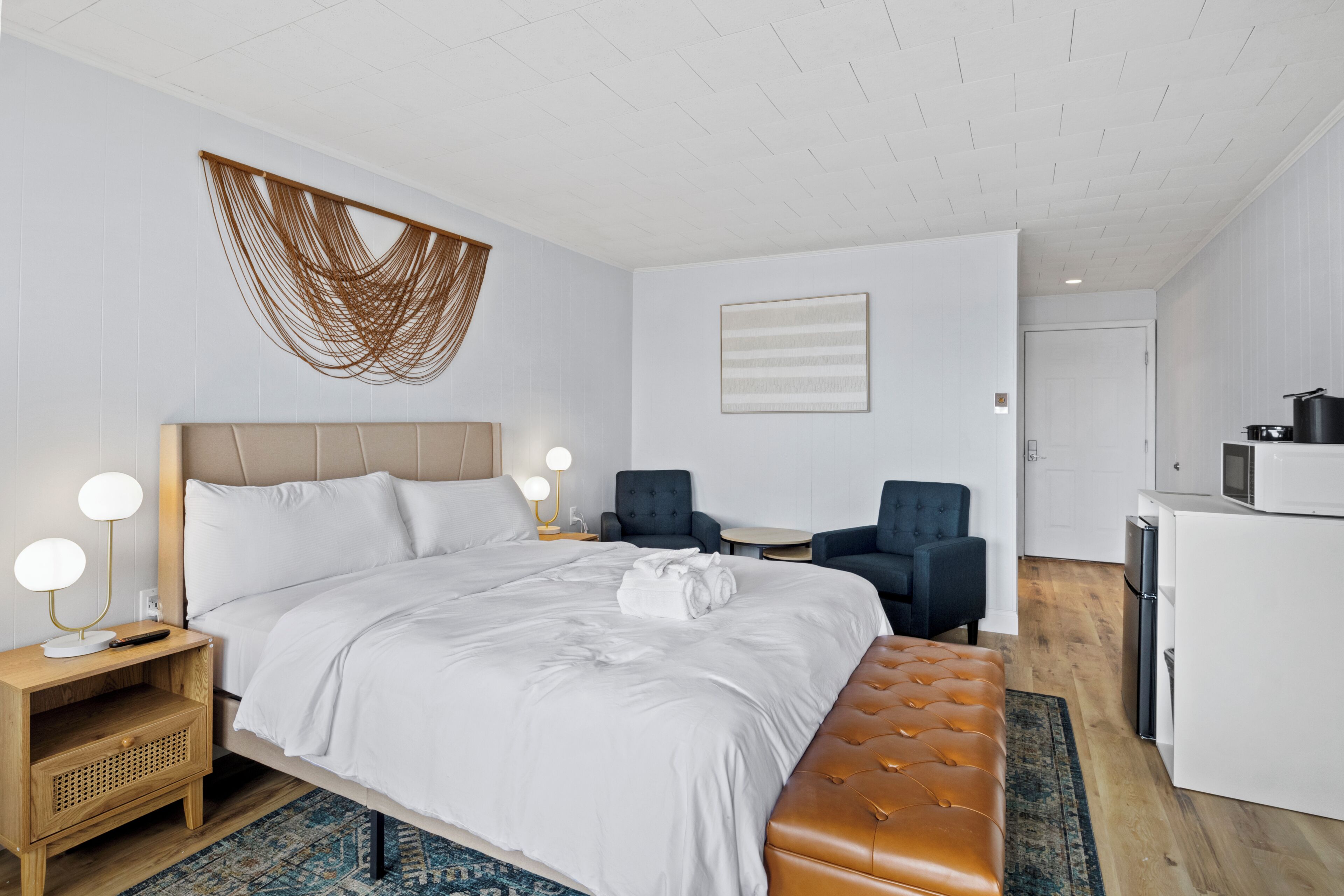 Una habitación de hotel moderna con una cama grande, mesitas de noche, un escritorio, una silla y una kitchenette.