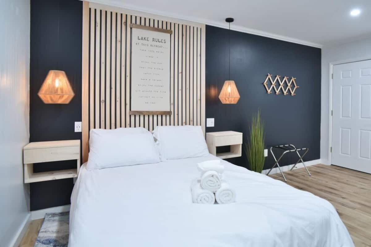 Un dormitorio moderno con una cama, dos mesitas de noche, una lámpara de pared, una puerta y una planta pequeña.