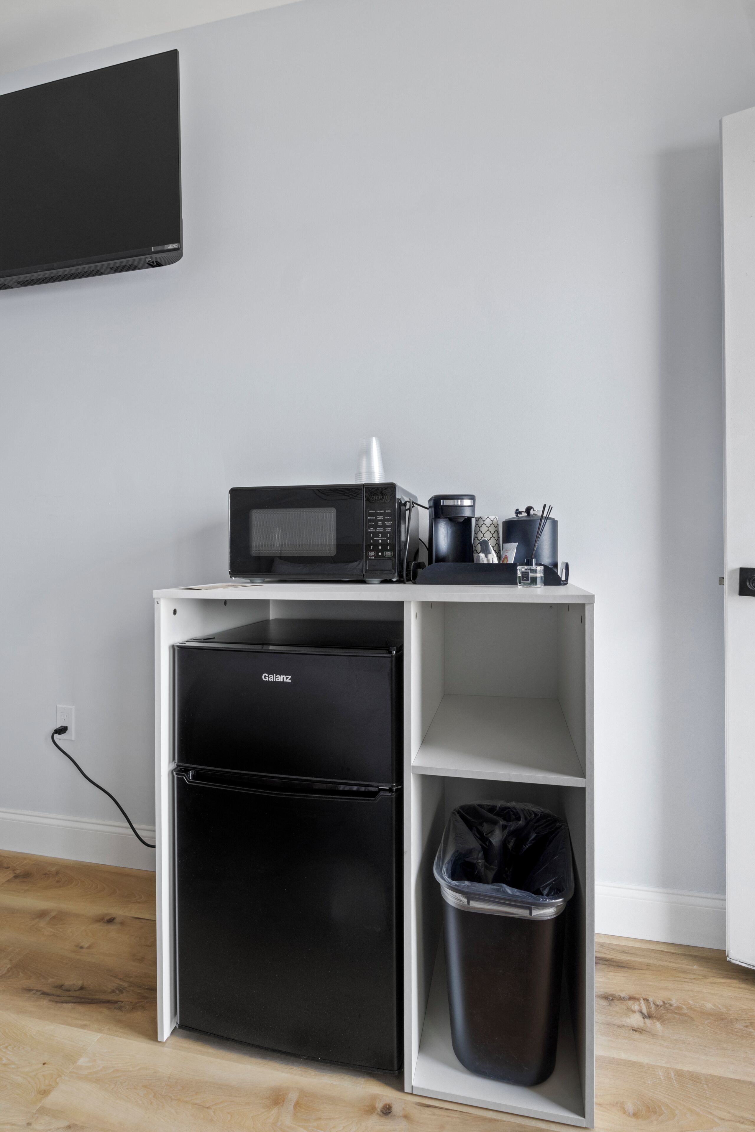 Una kitchenette con microondas, cafetera y cubo de basura.