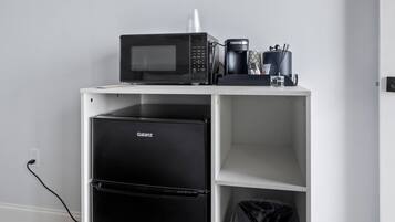 Una kitchenette con microondas, cafetera y cubo de basura.