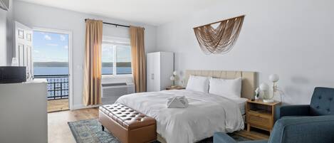 A hotel room with a bed, a seating area, a desk, and a view of the sea.