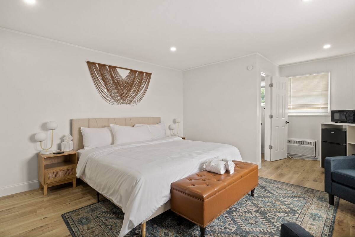 Un dormitorio con cama, mesita de noche, banco, escritorio y ventana.