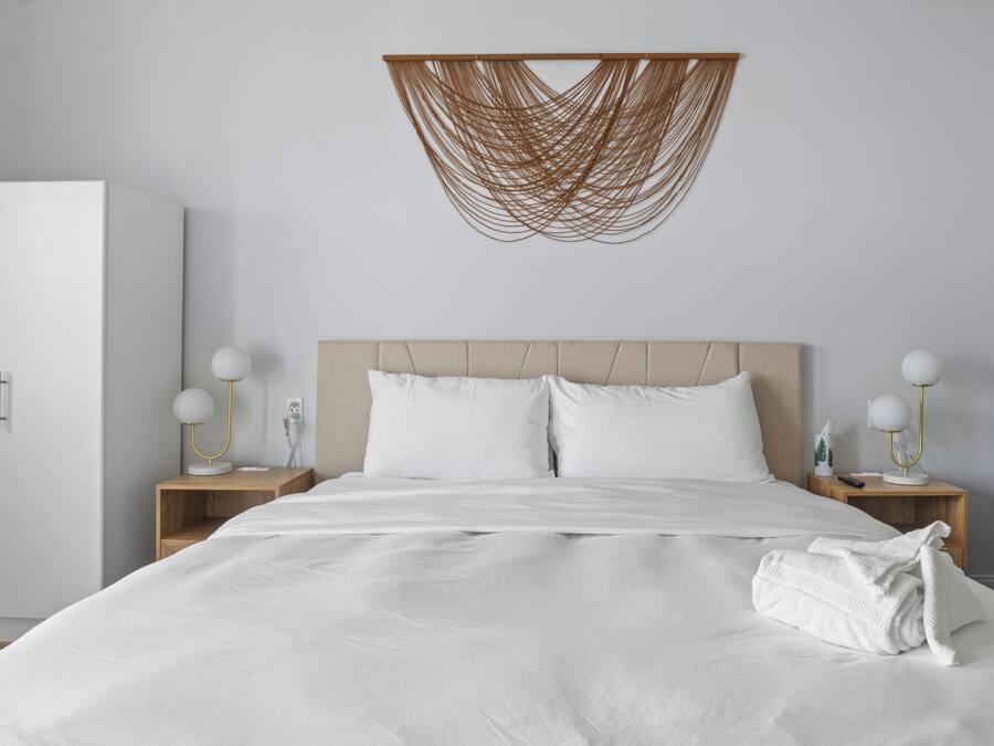 Una cama bien hecha con sábanas blancas, dos mesitas de noche con lámparas, un cabecero de madera y un sillón azul.