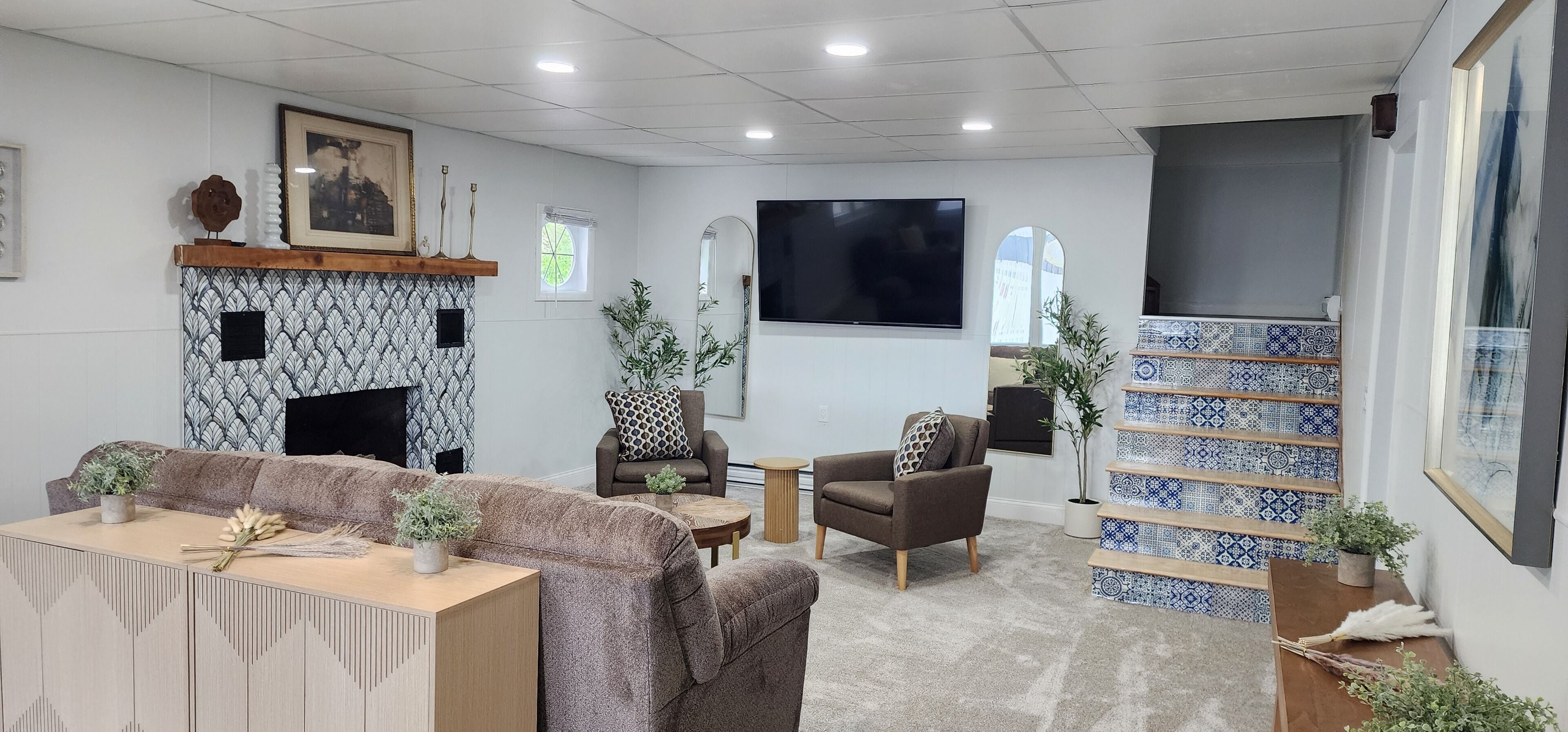 Una sala de estar moderna con chimenea, sofás, sillones, un televisor y una escalera con azulejos azules y blancos.