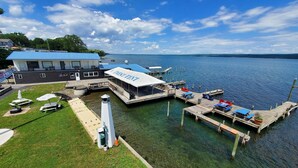 Un muelle a orillas del lago con un cobertizo para botes, una zona cubierta con carpas y un faro.