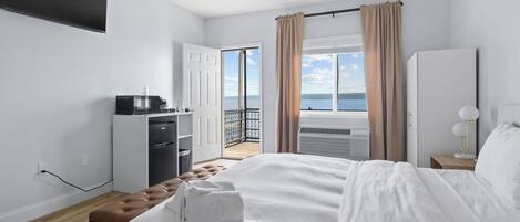 A bedroom with a bed, a desk, a wardrobe, a TV, and a balcony with curtains.