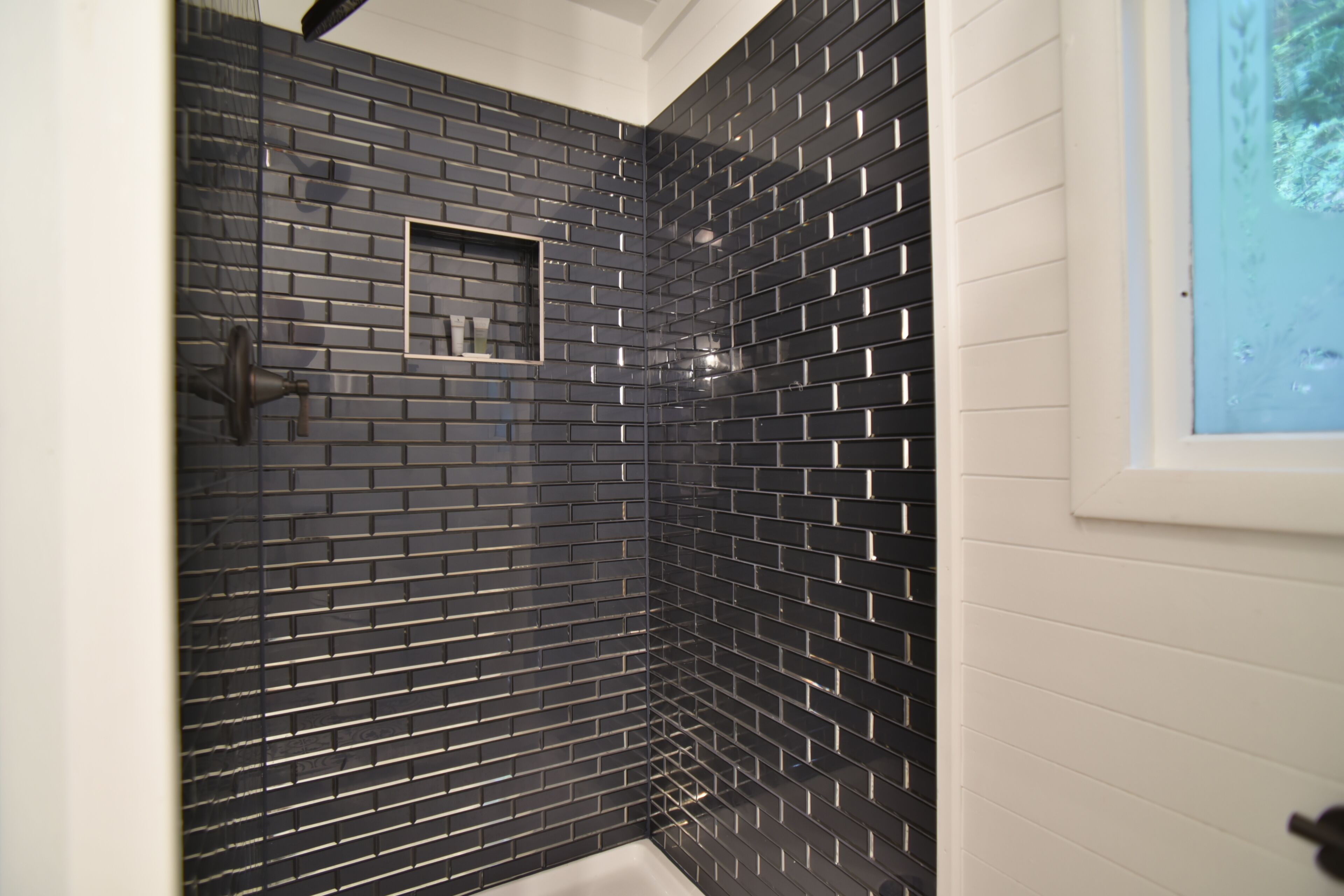 Ein Badezimmer mit schwarzen Fliesen an den Wänden, einer weißen Badewanne und einem gerahmten Bild.