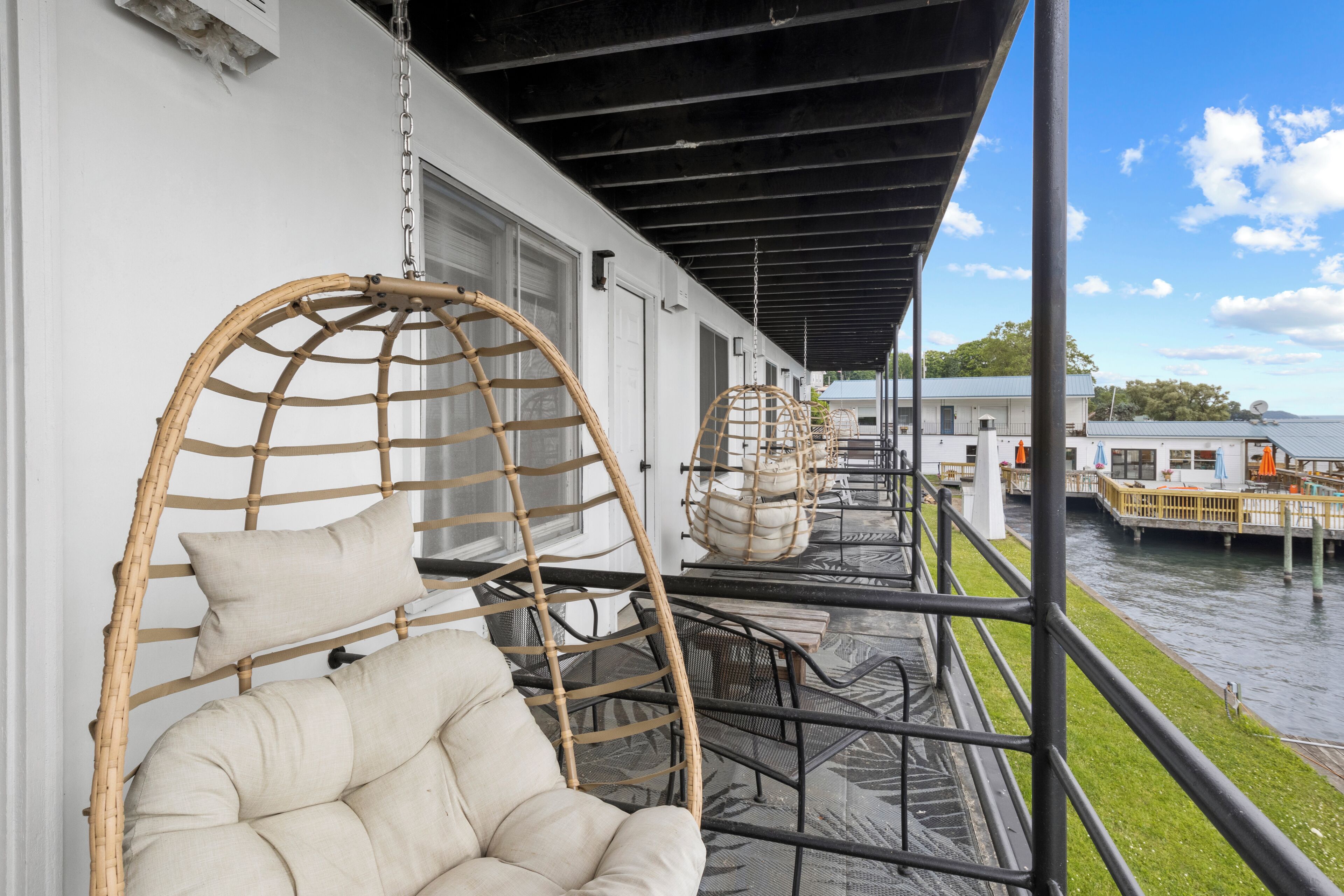 Un balcon avec des fauteuils en osier et un banc rembourré, donnant sur une étendue d’eau.