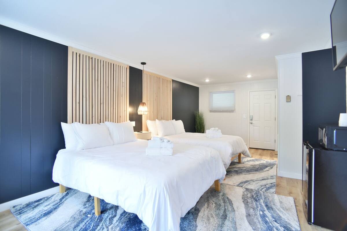 Habitación de hotel con dos camas, un panel de pared de madera, un ventanal grande y un refrigerador.