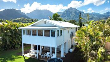 A white two-story house with a covered patio, a hot tub, and a view of mountains.