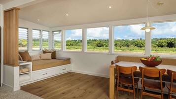 A room with a large window, a wooden bench, a dining table with chairs, and a hanging light fixture.