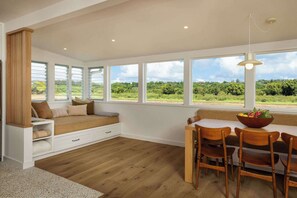 A room with a large window, a wooden bench, a dining table with chairs, and a hanging light fixture. - Cottage Four - Luxury Riverfront Stay on Kauai (Hanalei)