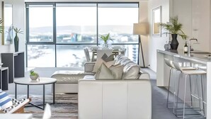 A modern living room with a sofa, a dining table, and a kitchen area with bar stools. - Scenic View 2 Bedroom Apartment - Pools, Gym and Secure Parking (Surfers Paradise)
