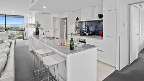 A modern kitchen with a central island, bar stools, and a view of the city. - Scenic View 2 Bedroom Apartment - Pools, Gym and Secure Parking (Surfers Paradise)