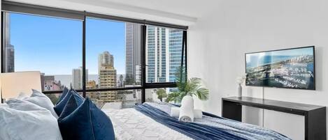 Een moderne slaapkamer met een groot bed, stadszicht, een flatscreen-tv en een bureau.