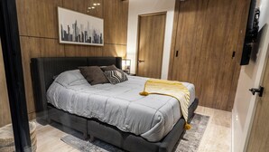 Une chambre moderne avec un grand lit, une œuvre d’art représentant un paysage urbain, un lambris en bois et une porte.