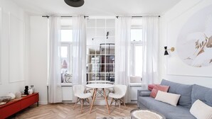 Ein modernes Wohnzimmer mit Fischgrätparkett, einem runden Couchtisch, einem grauen Sofa und einer roten Konsole.