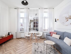 En moderne stue med fiskebensparket, et rundt sofabord, en grå sofa og et rødt konsolbord.