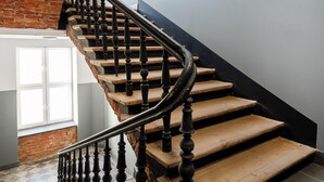 Eine Treppe mit Holzdielen und schwarzen Spindeln, die zu einer Zwischenebene mit einer weißen Tür und einer Ziegelwand führt.