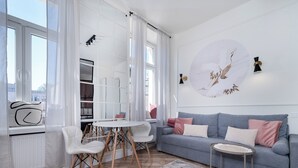 Ein modernes Wohnzimmer mit einem grauen Sofa, weißen Stühlen, einem runden Tisch und einem großen Fenster mit transparenten Vorhängen.