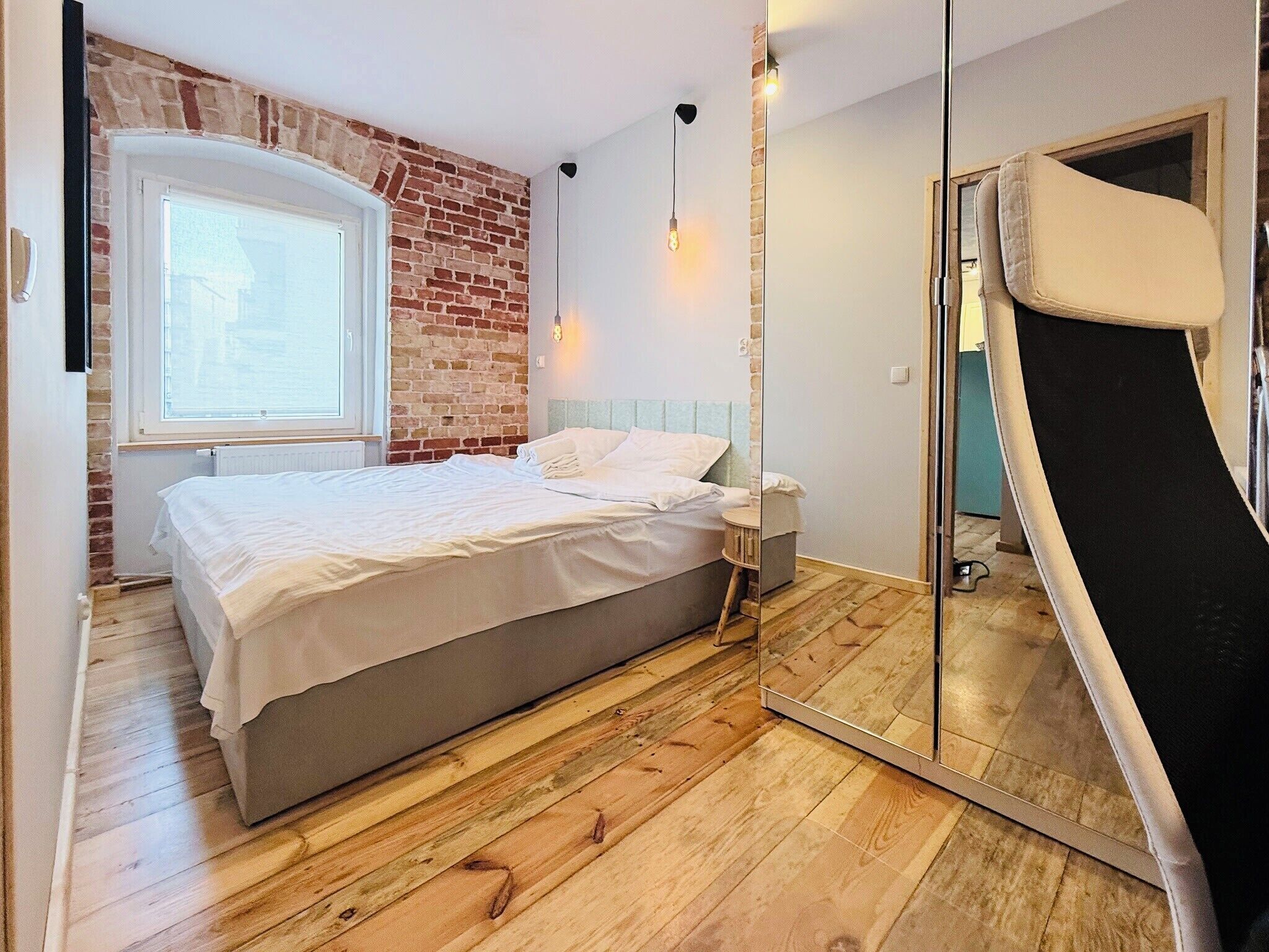 Une chambre avec un mur en briques, un lit, une table de chevet et une porte coulissante.