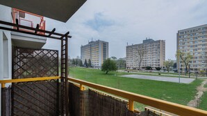 Ein Balkon mit Blick auf eine Rasenfläche, einen Metallzaun und hohe Wohnhäuser im Hintergrund.