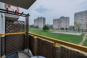 Un balcón con vista a un área verde, una cerca de metal y edificios residenciales altos al fondo.
