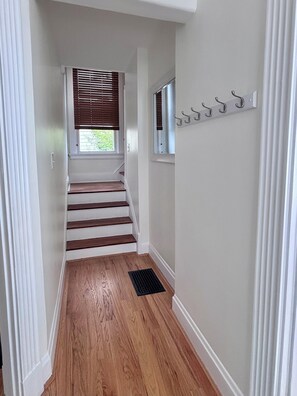 A hallway with wooden stairs, a window with blinds, and a coat rack with hooks. - Charming  Covington House. (Covington)