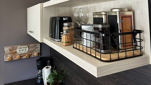 A kitchen with wooden shelves, a coffee maker, a toaster, and a blue colander. - Botanical Study 1 (San Carlos de Bariloche)