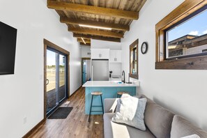 A narrow hallway leading to a kitchen with a central island, a sofa with a cushion, and a clock on the wall. - Dune View Lodge direct dune access (Saint Anthony)