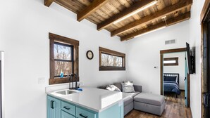 Cocina moderna con una isla grande, zona de comedor con sofá y dormitorio con cama y ventana.