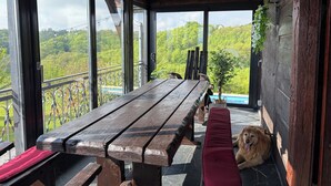 Um banco de madeira com almofada vermelha, um cão e vista para uma paisagem verde através de grandes janelas.
