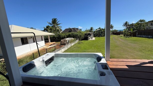 Ein Whirlpool auf einer Holzterrasse mit Blick auf einen grünen Garten und Häuser im Hintergrund.