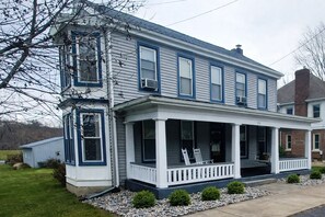 A two-story house with a porch, a garage, and a brick chimney. - This Old House / Cozy 3 BR near Sayers Lake (Howard)