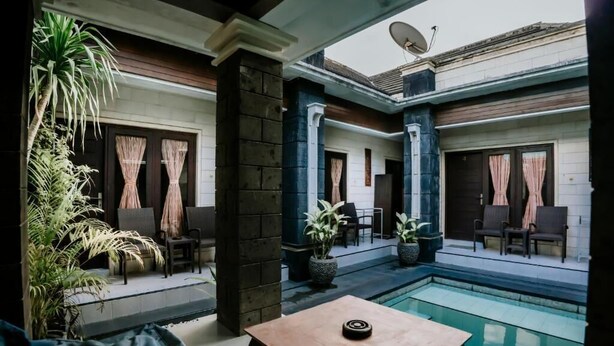 A poolside area with seating, a table, and potted plants. - Denays Guest House Jimbaran (Jimbaran)
