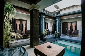 Zona junto a la piscina con asientos, una mesa y plantas en macetas.