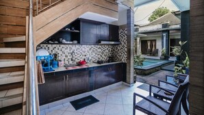 A modern kitchen with dark cabinetry, a tiled backsplash, and a view of an outdoor pool area. - Denays Guest House Jimbaran (Jimbaran)