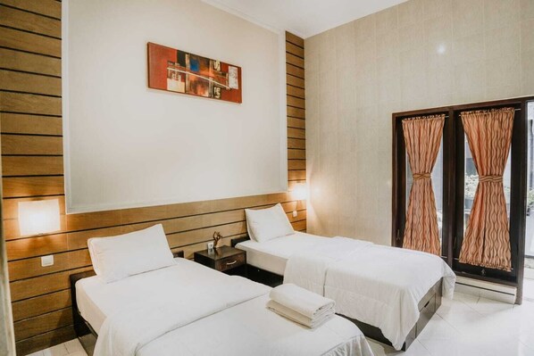 Habitación de hotel con dos camas, cabecera de madera, una obra de arte colgada en la pared y una ventana con cortinas.