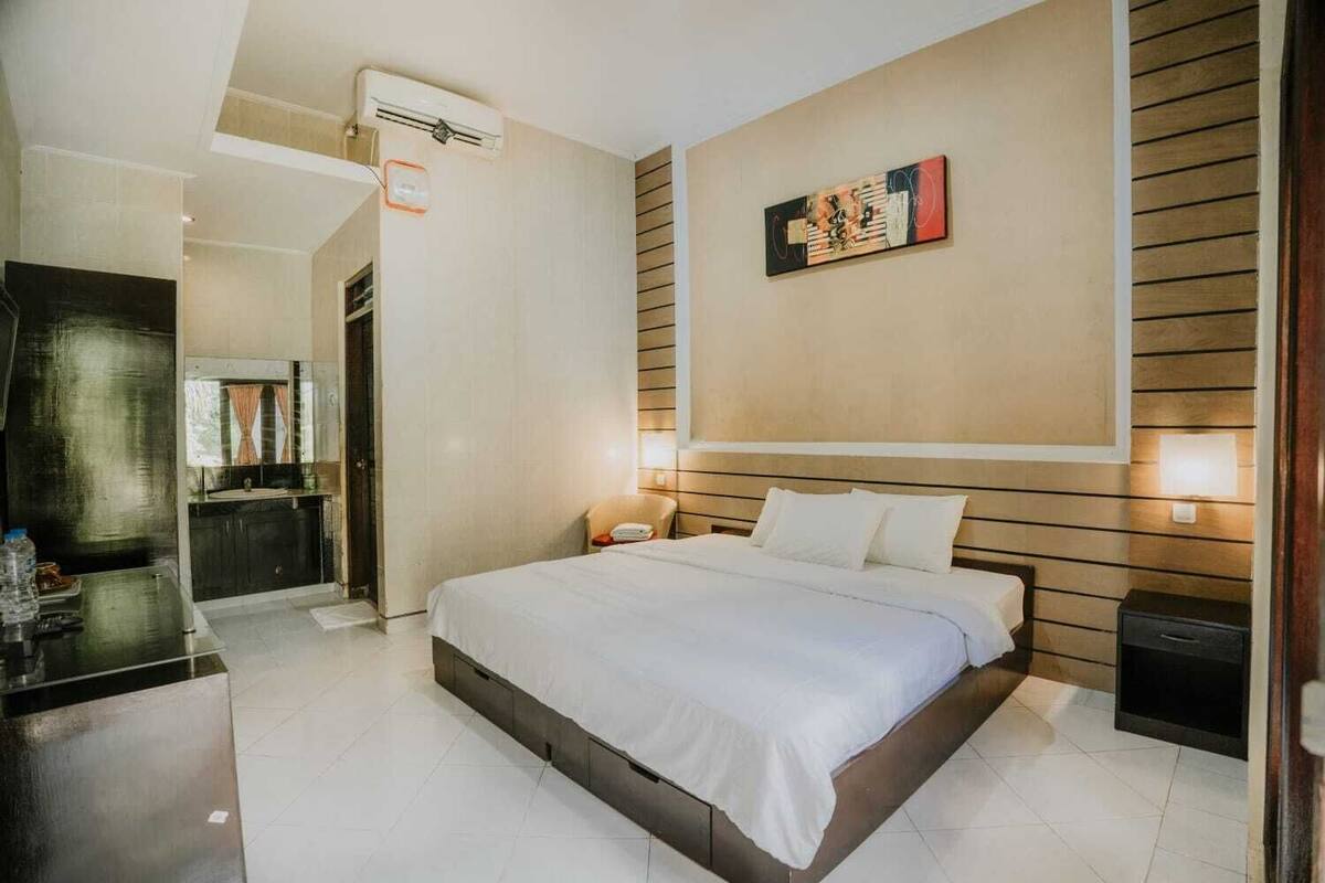 A hotel room with a bed, bedside table, wall-mounted artwork, and a bathroom visible through an open door.