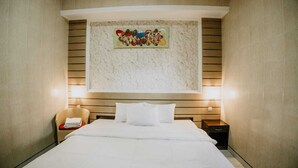 A hotel room with a bed, a headboard, a nightstand, a chair, and a wall-mounted artwork. - Denays Guest House Jimbaran (Jimbaran)