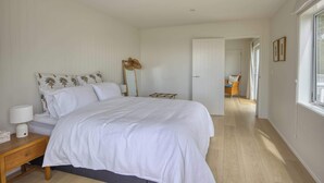 Een slaapkamer met een bed, nachtkastje, lamp en een deur naar een andere kamer.