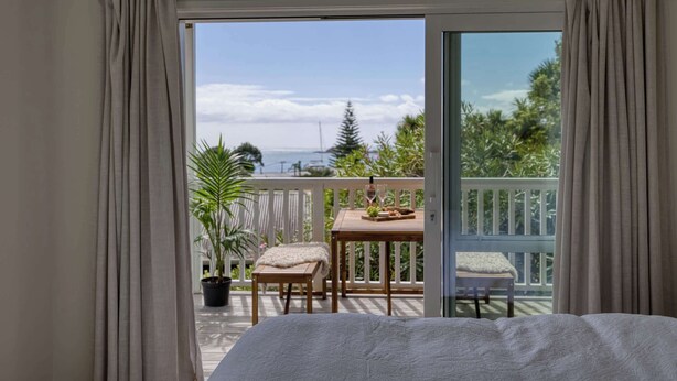 Een slaapkamer met een groot bed, een balkon met een tafel en stoelen, en uitzicht op zee.