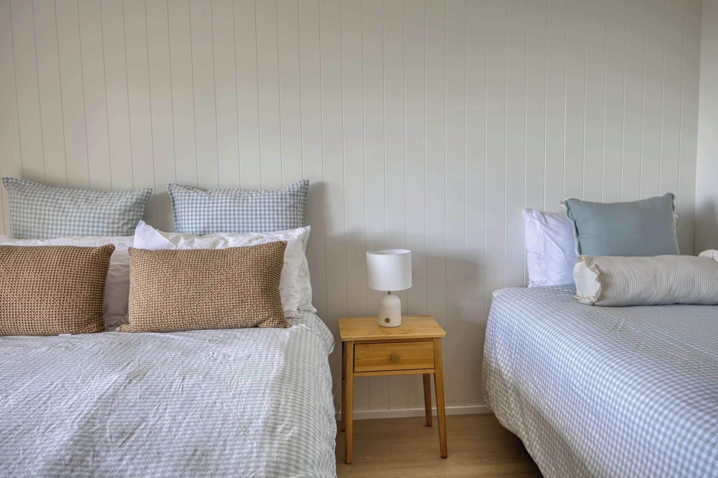 A bedroom with two beds, a nightstand with a lamp, and a wall with vertical lines.